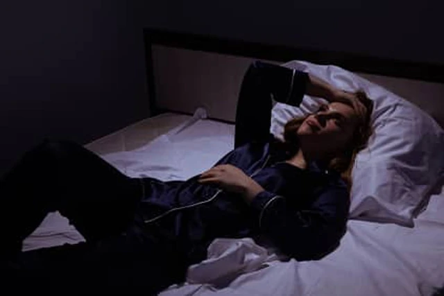 夜间躺在床上抬手遮住眼睛的人