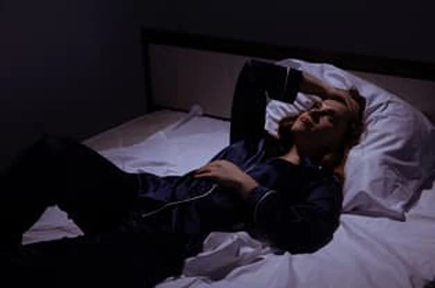 夜间躺在床上抬手遮住眼睛的人